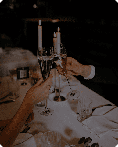 Toasting champagne glasses over candlelit dinner.