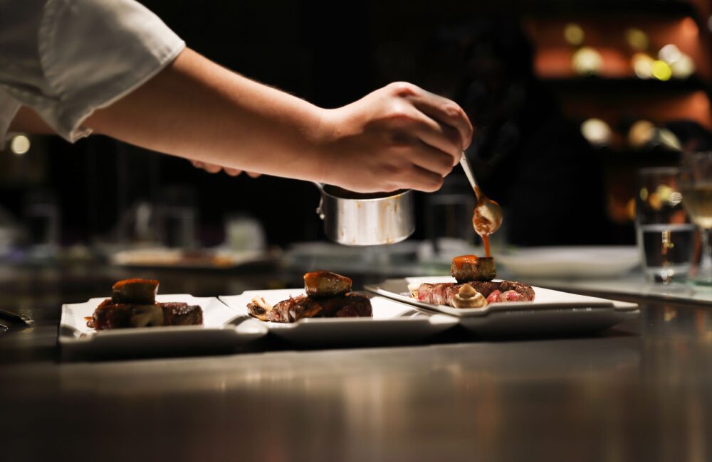 Chef plating gourmet dishes in dim light.