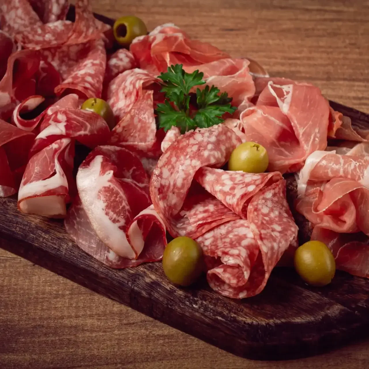 A wooden board with assorted cured meats and olives.